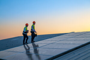 Image of two construction workers on a rooftop inspecting solar panels.