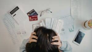 Overhead view of a stressed business person with head in hands surrounded by financial documents, bills, and a calculator, representing the burden of rising electricity costs on South African businesses