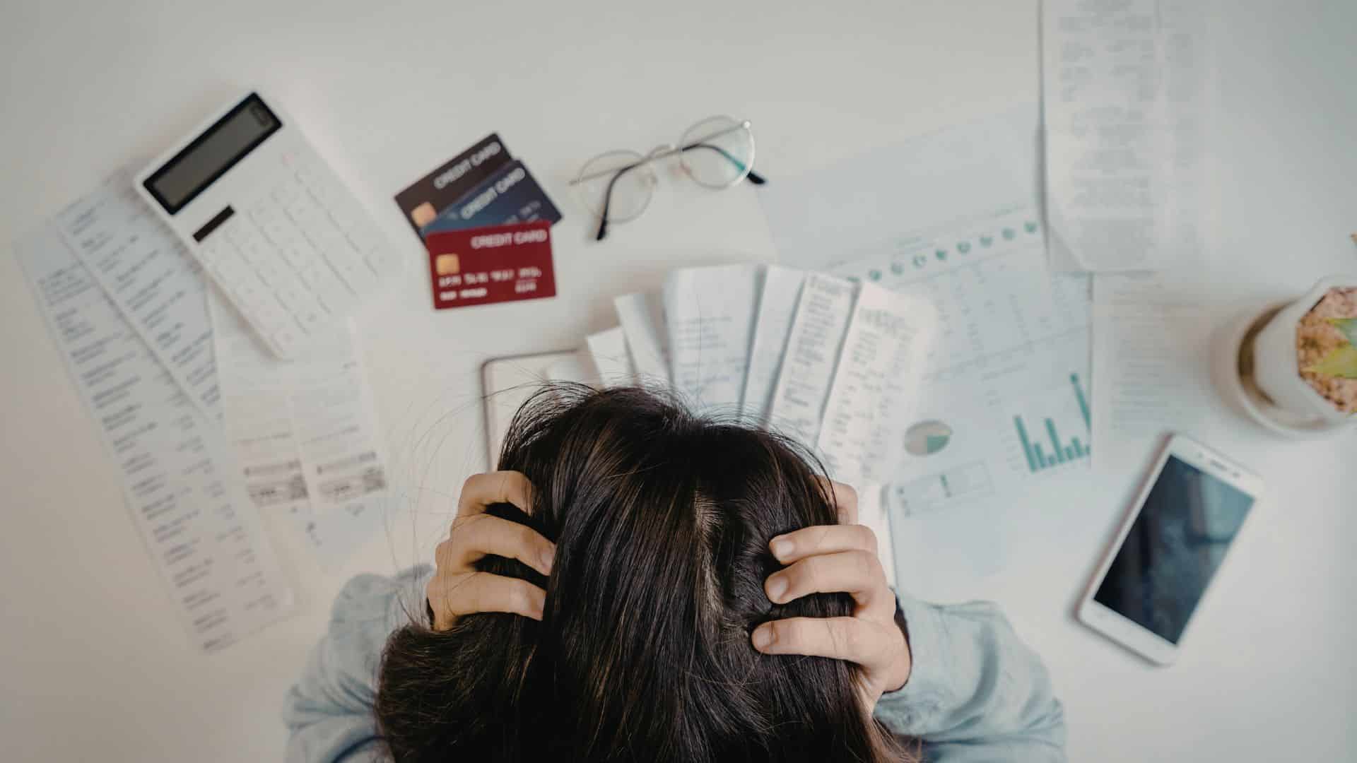 Overhead view of a stressed business person with head in hands surrounded by financial documents, bills, and a calculator, representing the burden of rising electricity costs on South African businesses