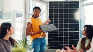 A solar sales representative presenting a solar panel to potential business clients in a modern office setting, illustrating the installer-led sales approach that independent advisors help businesses navigate